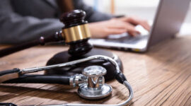 Close-up Of Mallet And Stethoscope On Gavel Over The Office Desk With Businessperson Using Laptop